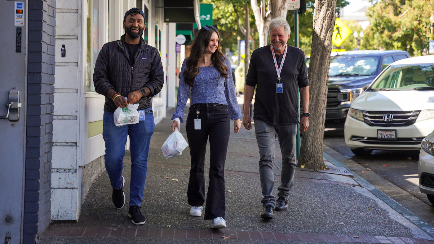 Three Genentech employees walk together in downtown SSF carrying food takeout from a local restaurant.